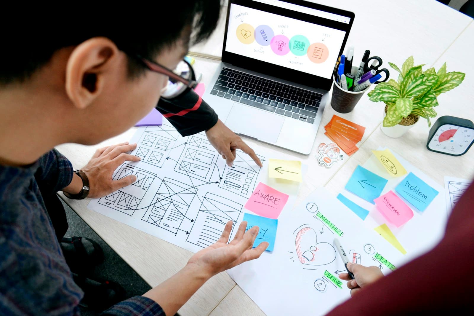 Designer sketching wireframes beside a laptop