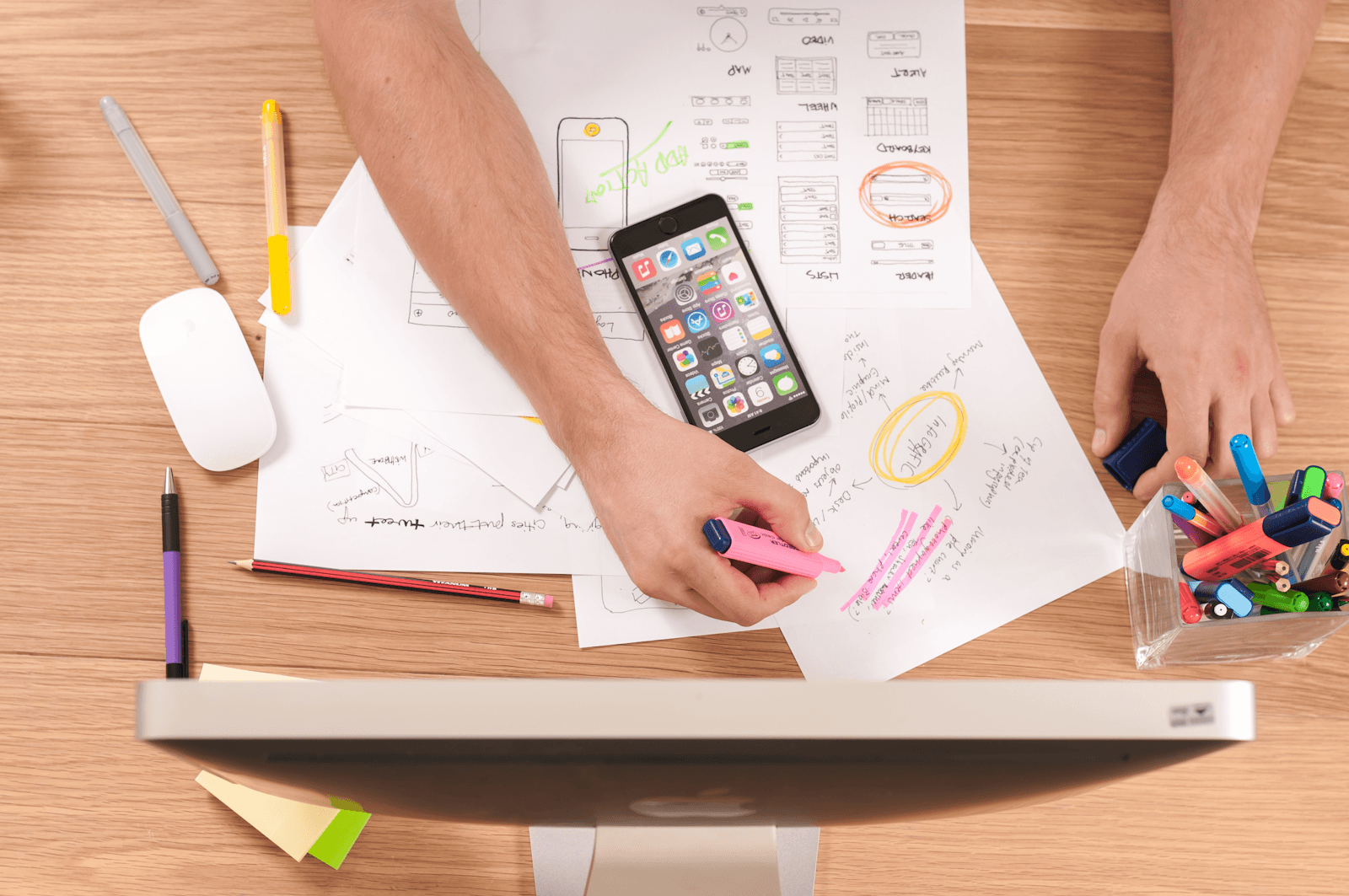 Wireframe sketches and a phone prototype on a designer's desk