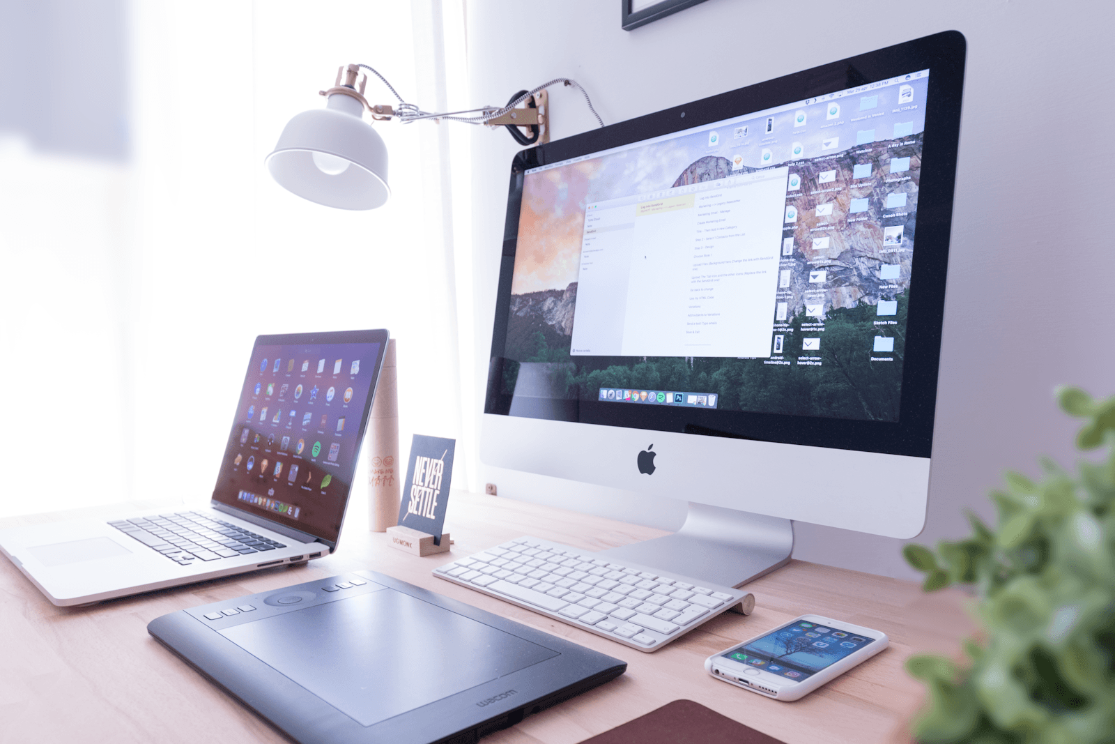 A designer's desk with a monitor, tablet and laptop